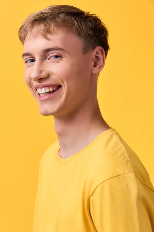 Smile, man, yellow background, casual shirt, warm lighting, upbeat mood, modern style, studio setup, everyday fashion, bright color theme, confident expression, clean composition, cheerful energy