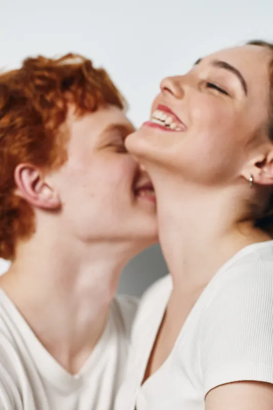 Young couple in love smiling and enjoying intimate moment together indoors. Man with red hair kisses woman smiling happily with closed eyes in closeup portrait of affection.