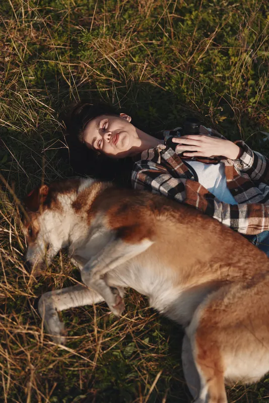 Girl and dog resting together in a sunny field, lying on grass with a joyful smile, capturing a relaxed outdoor moment of companionship and natural, carefree happiness perfect for lifestyle stock