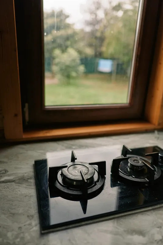 Gas stove burner on a kitchen counter beside a window, showcasing a quiet domestic scene with natural light, reflective metal surface, and simple home ambience