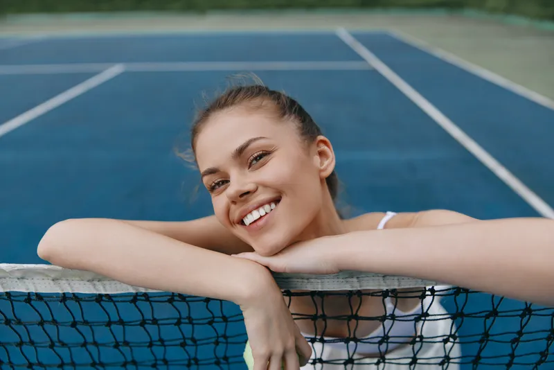 Smiling young woman enjoying tennis on a vibrant blue court, showcasing health and happiness, perfect for sports themed content
