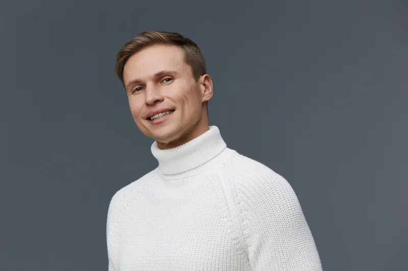 Smiling man wearing white knitted sweater standing isolated on gray background with modern casual style and confident posture for freelance work digital nomad concept