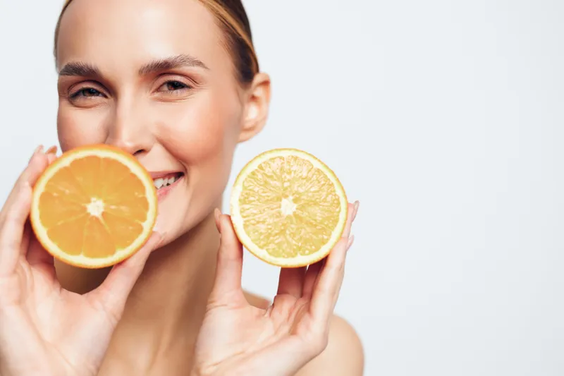 Smiling young woman holding two halves of citrus fruits near her face isolated on white background showing fresh organic oranges with healthy skin and natural beauty concept.