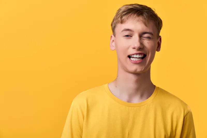 Smiling young man wearing a yellow shirt against a vibrant yellow backdrop, conveying a cheerful mood, casual style, and approachable vibe for lifestyle or advertising projects