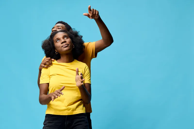 Happy young couple enjoying a playful moment together against a bright blue background, wearing yellow shirts, showcasing joy and connection