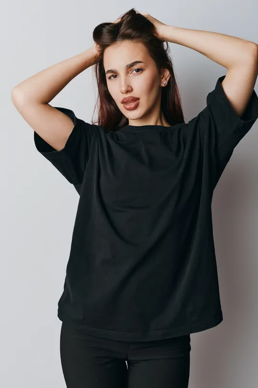 Young woman posing with hands in hair wearing black t shirt and pants against neutral background. Casual style, confident expression, beauty and fashion portrait with natural look.