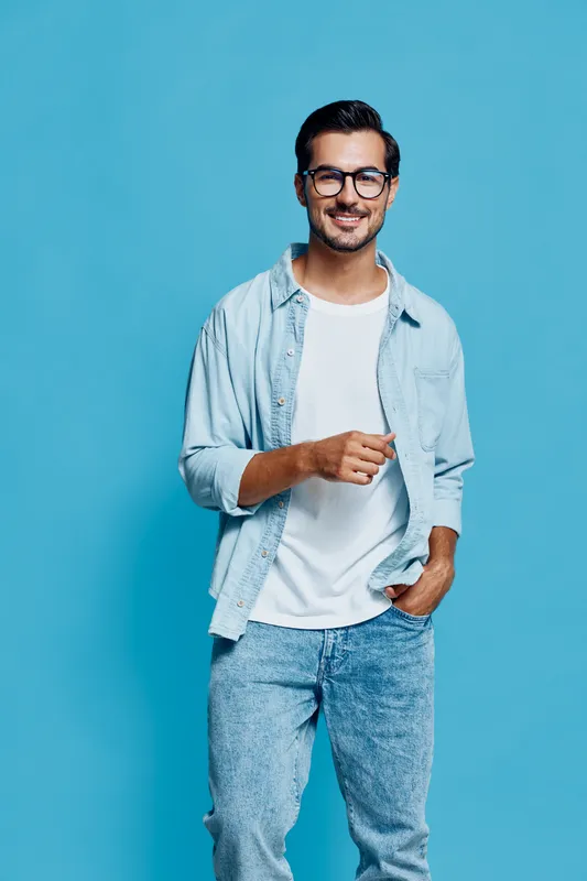 Smiling happy cheerful young man wearing a light blue shirt smiles at the camera while holding a pen, isolated on a solid light blue background. Lifestyle concept.