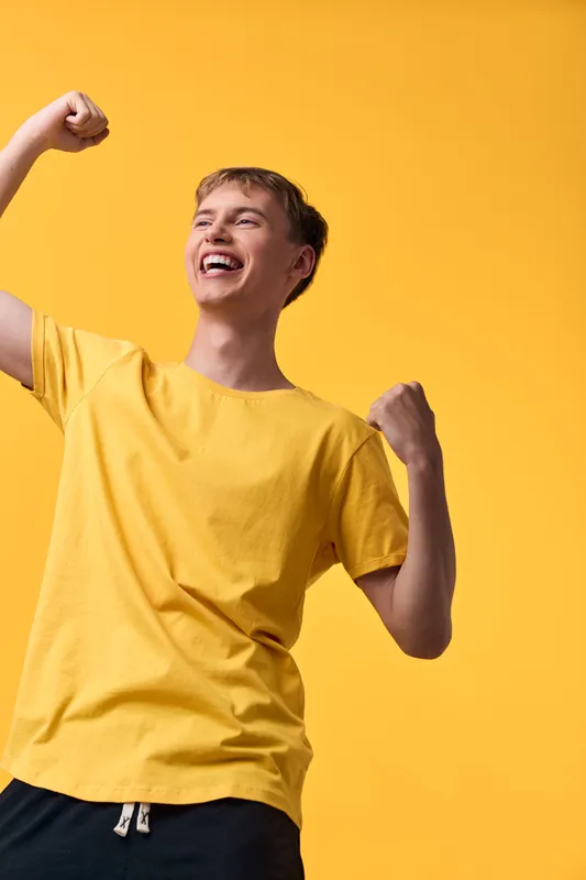 Joyful youth in a bright yellow shirt raises fists in celebration, exuding energy and happiness against a vivid backdrop, conveying optimism, momentum, and dynamic spirit for active lifestyle and