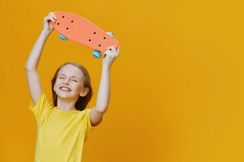 Happy young girl in a bright yellow t shirt celebrating with a skateboard, vibrant orange skateboard against a cheerful yellow background