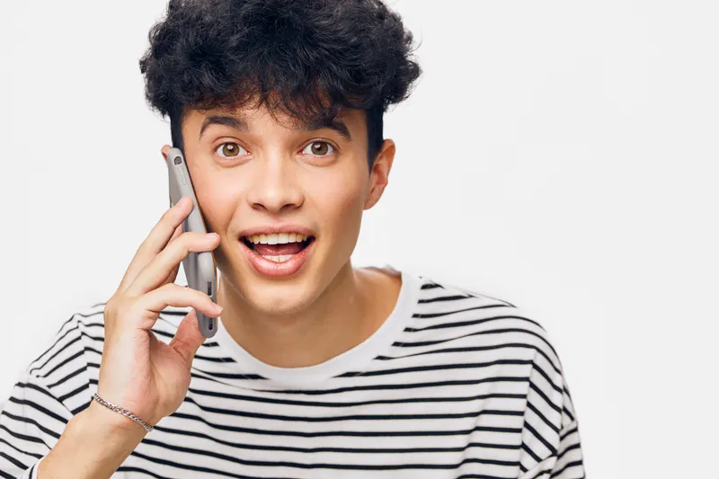 young man talking phone with surprised expression, casual striped shirt, curly hair, isolated on white background, communication concept