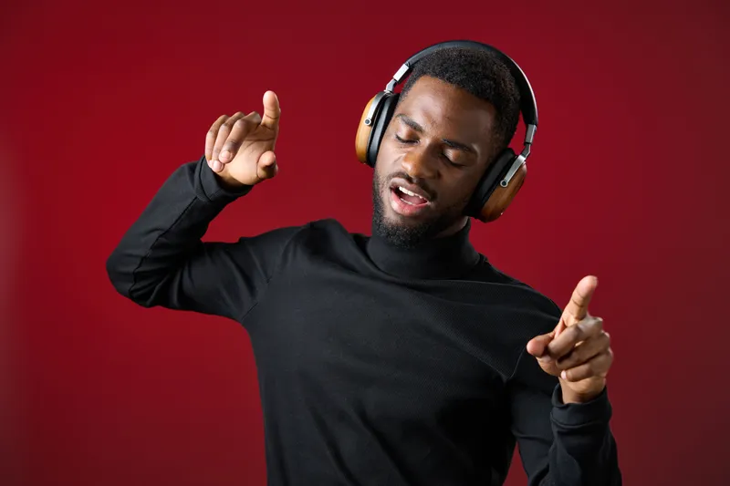 Young Black man enjoying music with headphones, dancing with joy against a vibrant red background, showcasing happiness and modern style