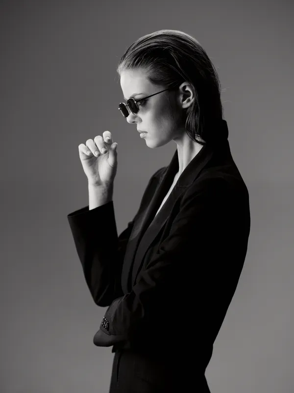 Black and white portrait of a thoughtful woman wearing sunglasses and a suit jacket in profile view.
