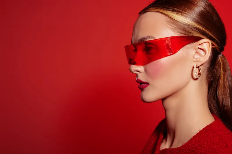 Profile of a stylish woman wearing red sunglasses and red clothing against a red background. Concept of fashion, beauty, and modern style with vibrant colors.
