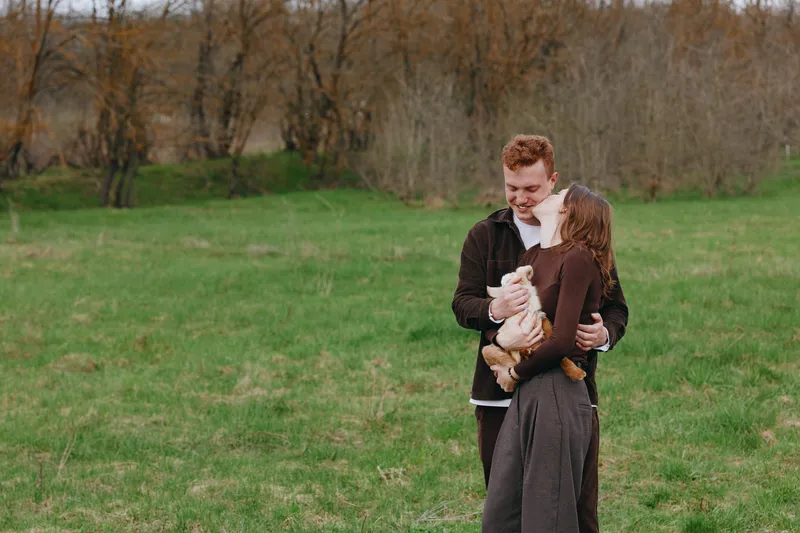 A couple outdoors in a field share a gentle embrace with a small dog, creating a natural lifestyle moment filled with affection and love in open countryside.