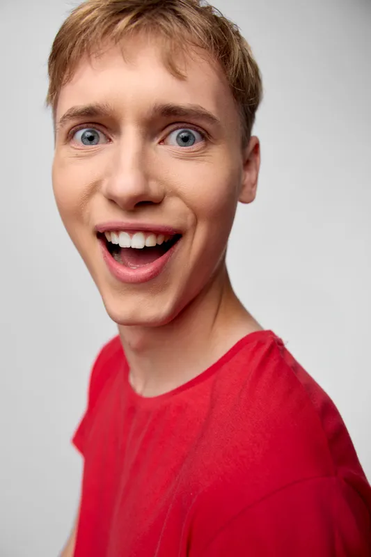 Surprised man in a red shirt with wide-eyed open-mouthed expression shows excitement, ideal for lifestyle and advertising campaigns, closeup shot that highlights facial features and energetic mood