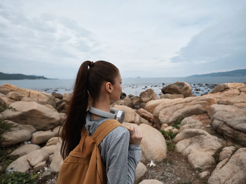 Young woman with a backpack enjoys a tranquil view of the rocky beach, reflecting on life s moments amidst nature and serenity