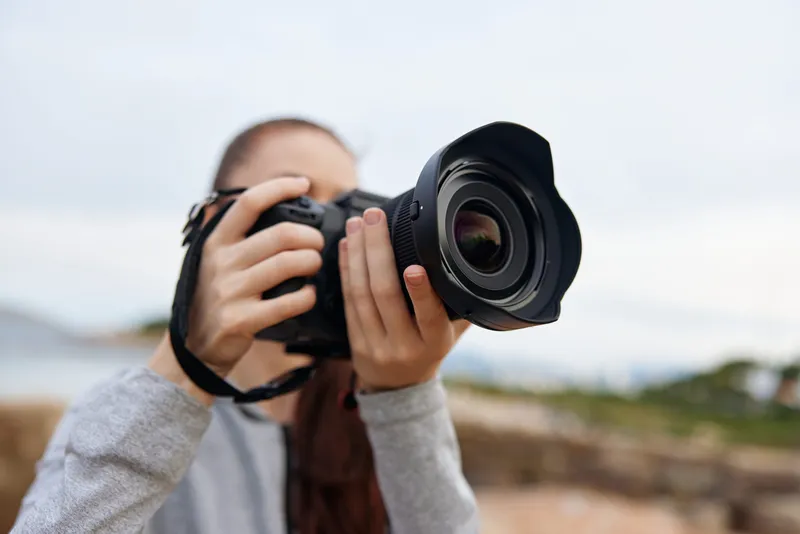 Young woman holding a professional camera outdoors, capturing nature with a focused expression, showcasing photography passion and creativity in a serene environment