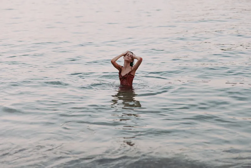 Young woman standing in calm sea water wearing a red swimsuit, enjoying peaceful ocean waves during a warm day at the beach.