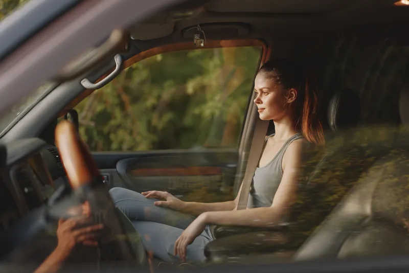 Young woman relaxing in car, enjoying nature views, with sunlight creating a warm ambiance and soft reflections on the window, embodying a peaceful moment