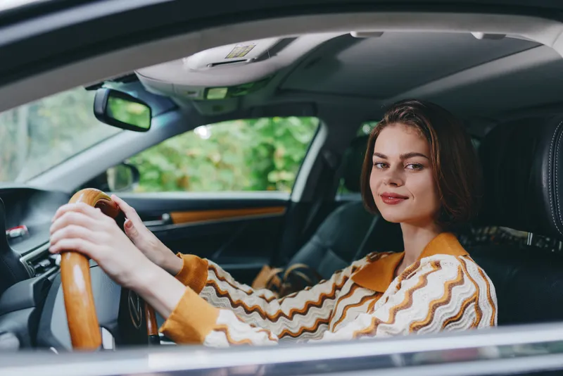 Car, driver, woman, smile a cheerful woman sits in the driver's seat with her hand on the steering wheel, radiating joy, confidence, and readiness for a journey ahead.