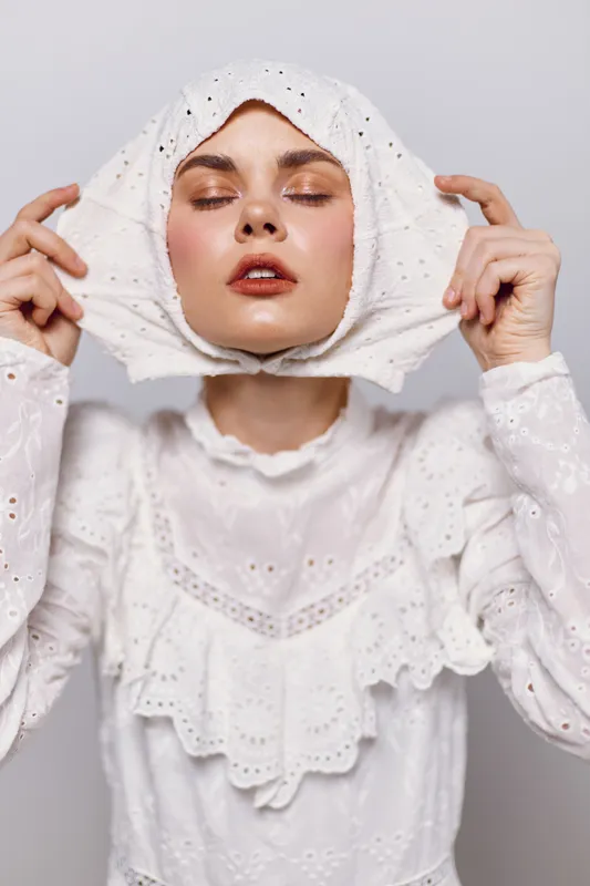 Woman in a white lace dress holding her face, showcasing emotion and style, ideal for concepts related to fashion and beauty