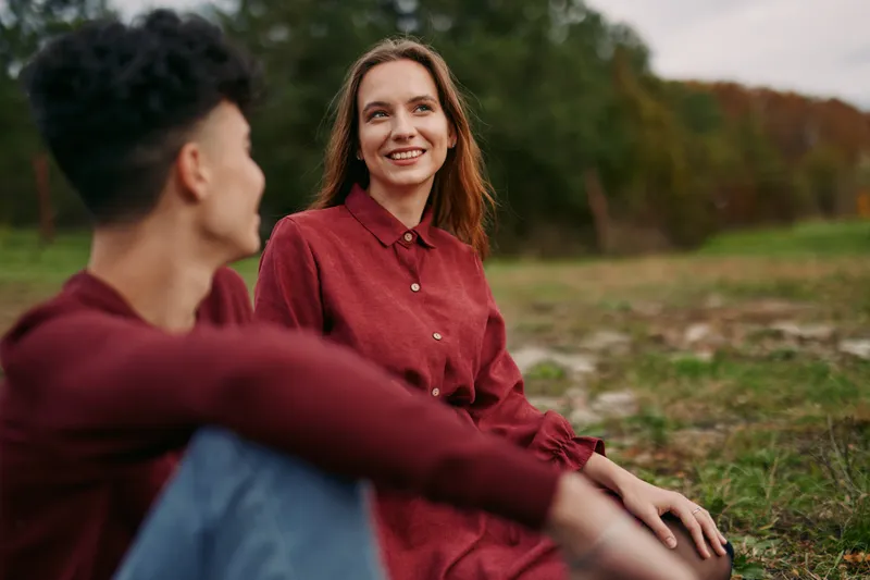 Candid portrait of a smiling woman sharing a genuine moment with a friend outdoors, natural light and relaxed posture convey authenticity and trustworthy human connection.