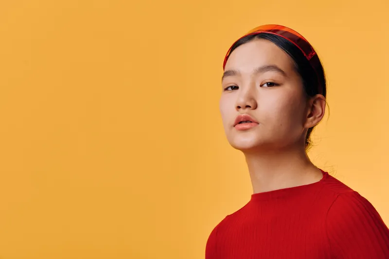 Young woman in red sweater and headband posing against yellow background looking confident and thoughtful with minimalistic style and clean backdrop in portrait shot.