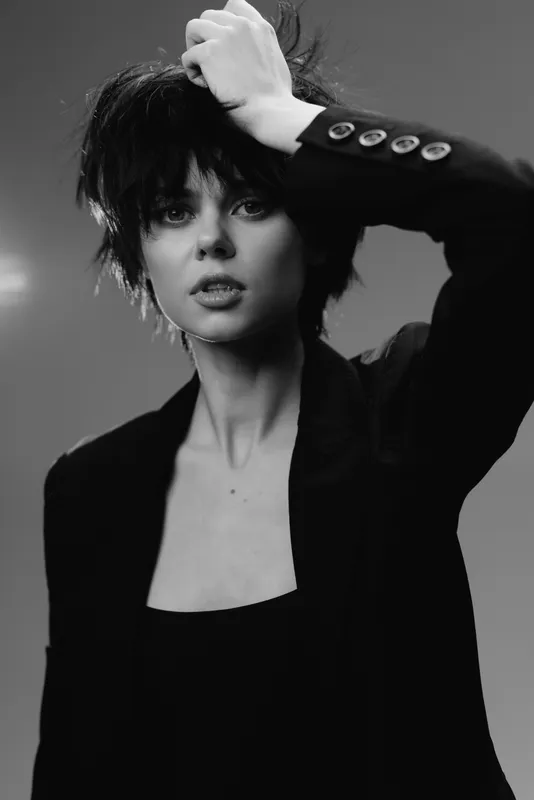 Black and white portrait of a stylish woman with short hair wearing a blazer expressing thoughtful emotion.