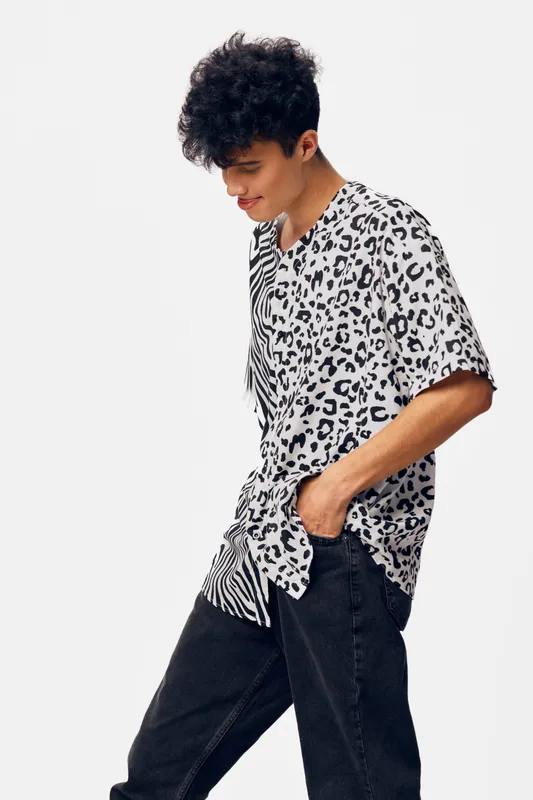 young man wearing a stylish black and white animal print shirt with black pants, standing in a casual pose with a neutral white background