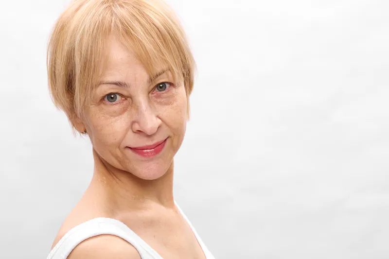 Closeup portrait of senior blonde woman with short hair and gentle smile, looking at camera in studio, white background, natural beauty calm headshot