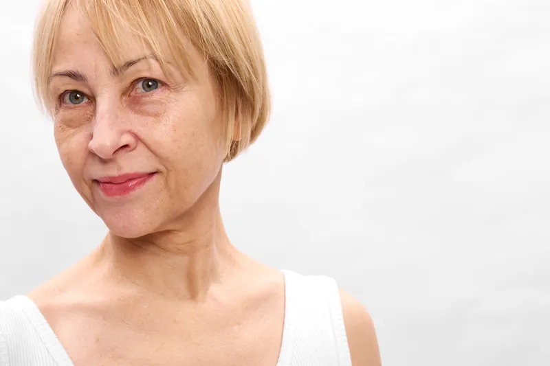 Senior blonde woman portrait, closeup face, calm gentle smile, natural skin texture, short hair style, soft studio lighting, white background, beauty confidence