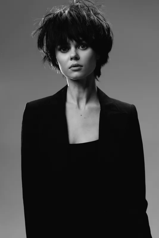Black and white portrait of a young woman with short messy hair wearing a dark blazer with a serious expression