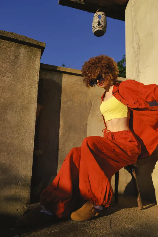 Dancer outdoor one person woman young curly hair yellow top orange suit posing on a sunlit rooftop with textured walls, showcasing confident street style and modern lifestyle