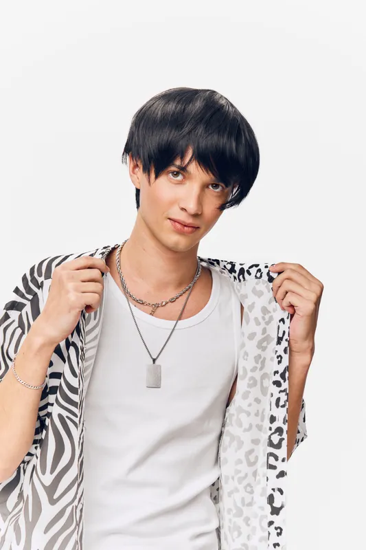 young man posing confidently wearing a patterned jacket and white shirt, short dark hair, silver necklace, looking directly at camera, isolated white background