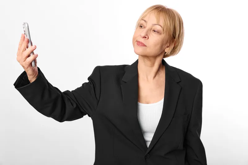 Woman senior in business suit holding smartphone for communication, technology portrait on white background, confident smile, copy space, studio lighting