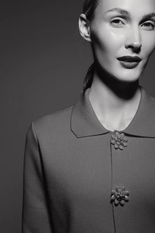 Portrait of a white European woman with fair skin wearing a vintage textured jacket with decorative buttons. Studio lighting highlights elegant facial features and hairstyle.