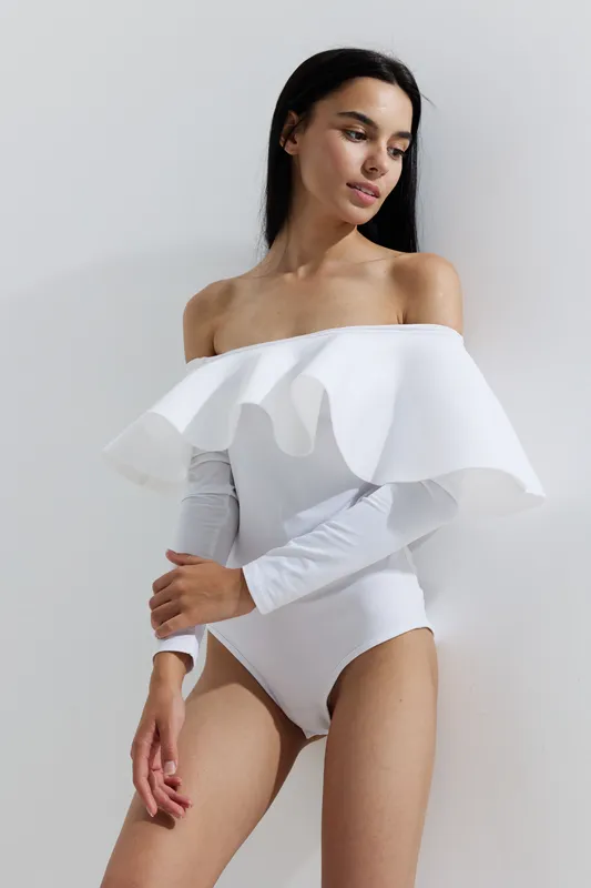 woman sport fitness in white athletic wear standing against bright wall, natural light highlighting toned arms and serene expression, modern minimal style