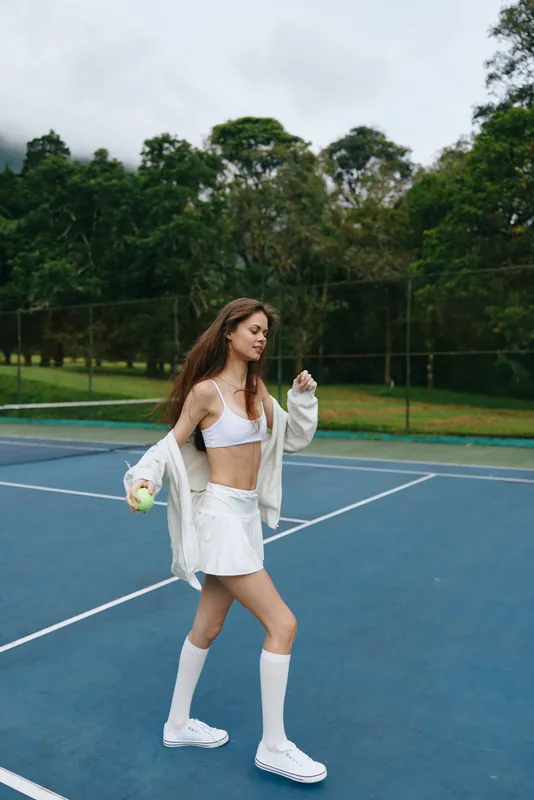 Young female athlete walking on a tennis court in sportswear, embodying energy and confidence, surrounded by greenery in a sporty atmosphere
