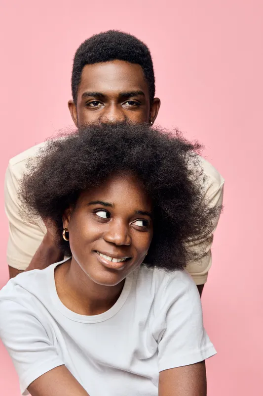 A joyful couple with natural hairstyle posing against a pink background, showcasing love, inclusivity, and modern relationships in a playful and vibrant style