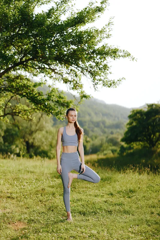 Young woman practicing yoga outdoors in a serene landscape, wearing activewear in soft colors, showcasing balance and tranquility in nature