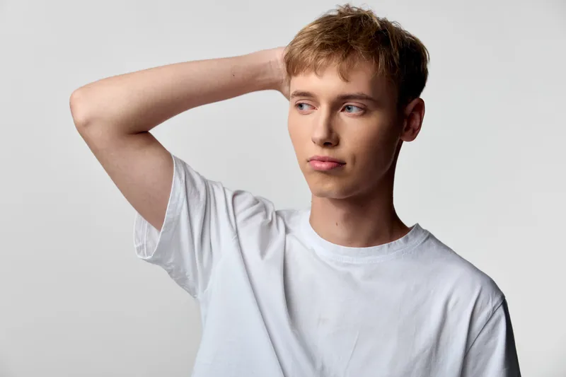Man with puzzled expression, hand on head, casual white tee, studio lighting, conveying confusion and contemplation for thinking, decision making, problem solving, and everyday uncertainty