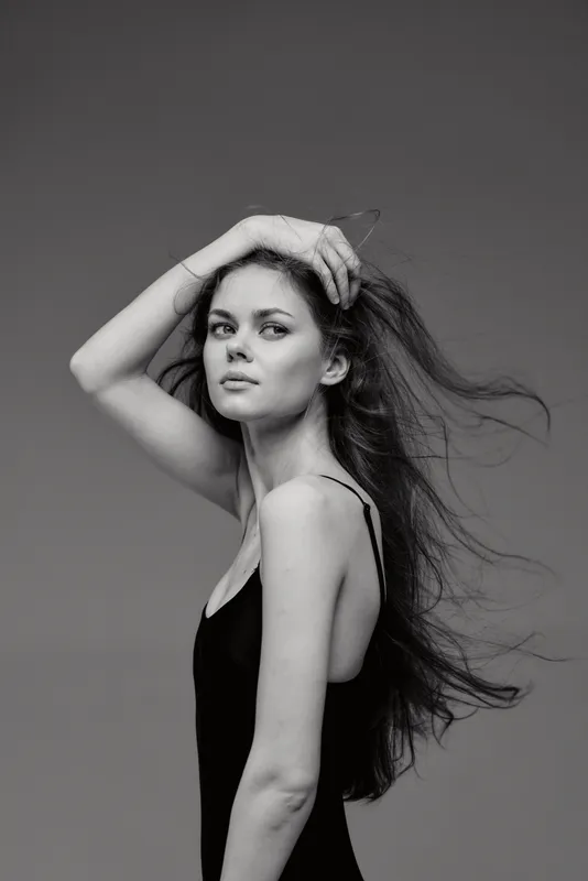 Black and white portrait of a young woman with flowing hair in a simple black dress expressing calm confidence.