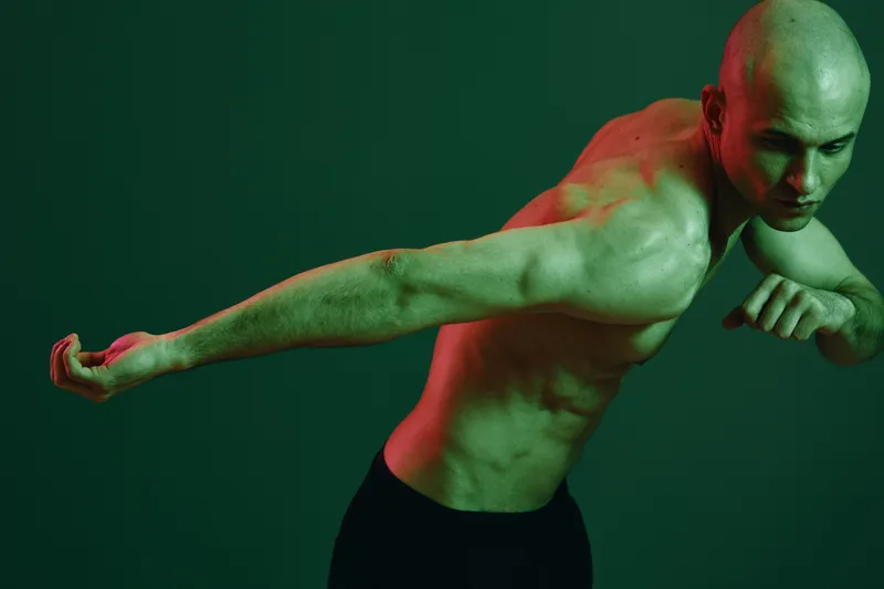 Dynamic man posing in dramatic lighting, showcasing strength and athleticism with an intense expression, emphasizing movement and power in the atmosphere.