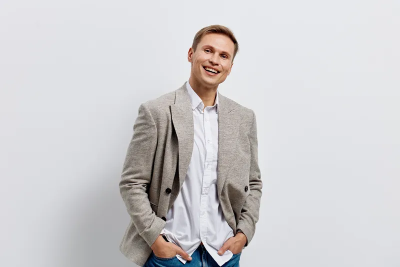 smiling man in casual white shirt beige jacket blue jeans standing relaxed isolated on grey background digital nomad concept lifestyle technology