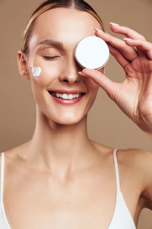 Woman beauty skincare routine, applying cosmetic cream on face, smiling and holding round compact, fresh makeup look, soft light on beige background