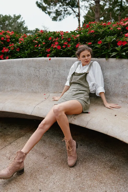 Young woman in casual summer outfit sitting outdoors, surrounded by vibrant flowers, expressing relaxed emotions, showcasing a fresh and stylish seasonal look