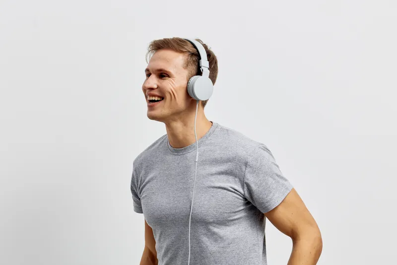 smiling young man wearing headphones listen music gray t-shirt isolated on light background digital detox concept
