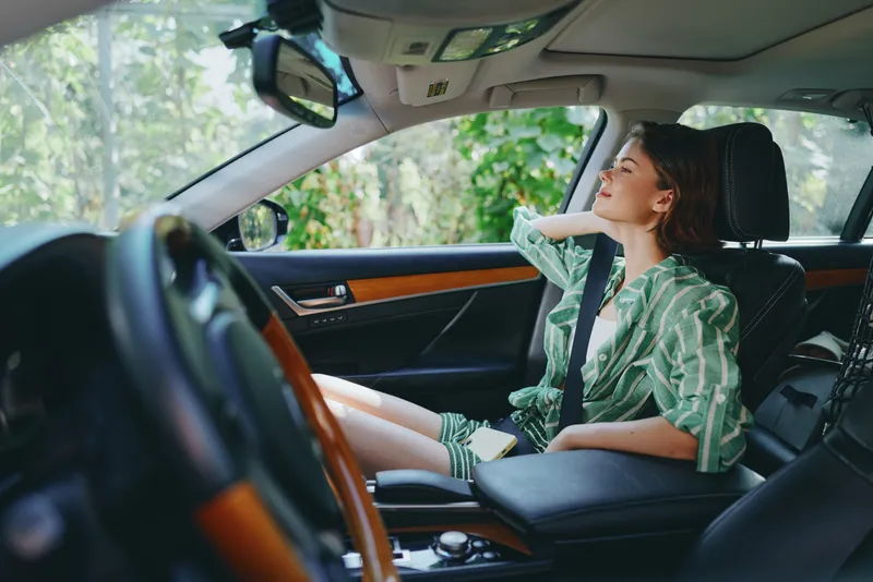 Young woman sits in a luxurious car interior, relaxed pose, natural light, green shirt, and confident gaze as she looks out the window.
