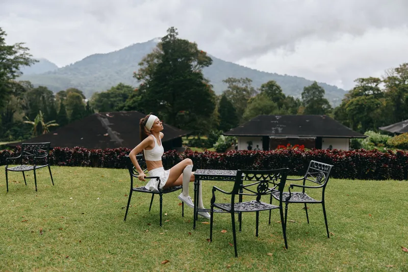 Young woman enjoying nature in a white outfit, sitting on garden chairs surrounded by mountains and greenery, reflecting relaxation and joy