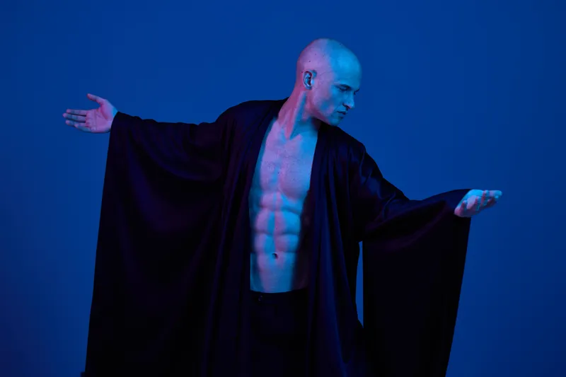 Muscular man striking a pose in dramatic black and white, showcasing strength and grace. The composition highlights his toned physique amidst a striking backdrop.